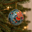 boule de noel artisanale bleue avec des fleurs peintes à la main, accrochée à une branche de sapin